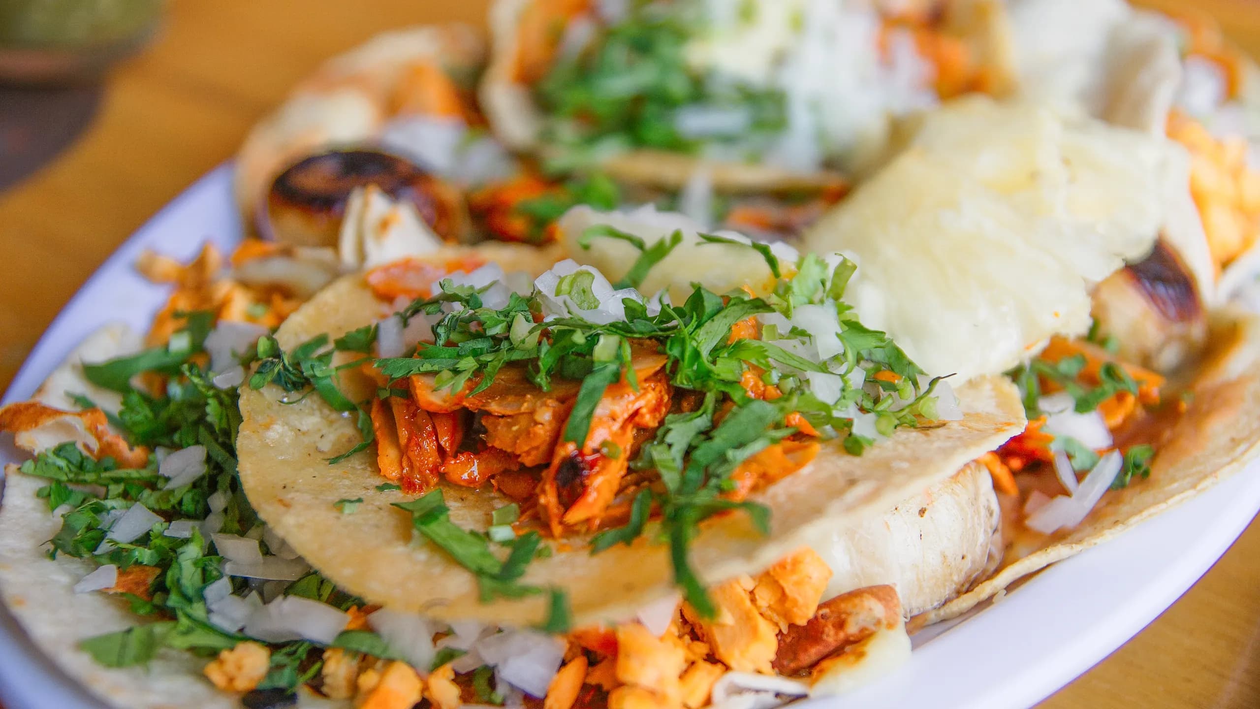 A platter filled with freshly assembled tacos al pastor topped with charred marinated pork, finely chopped cilantro, diced white onions, and slices of pineapple.
