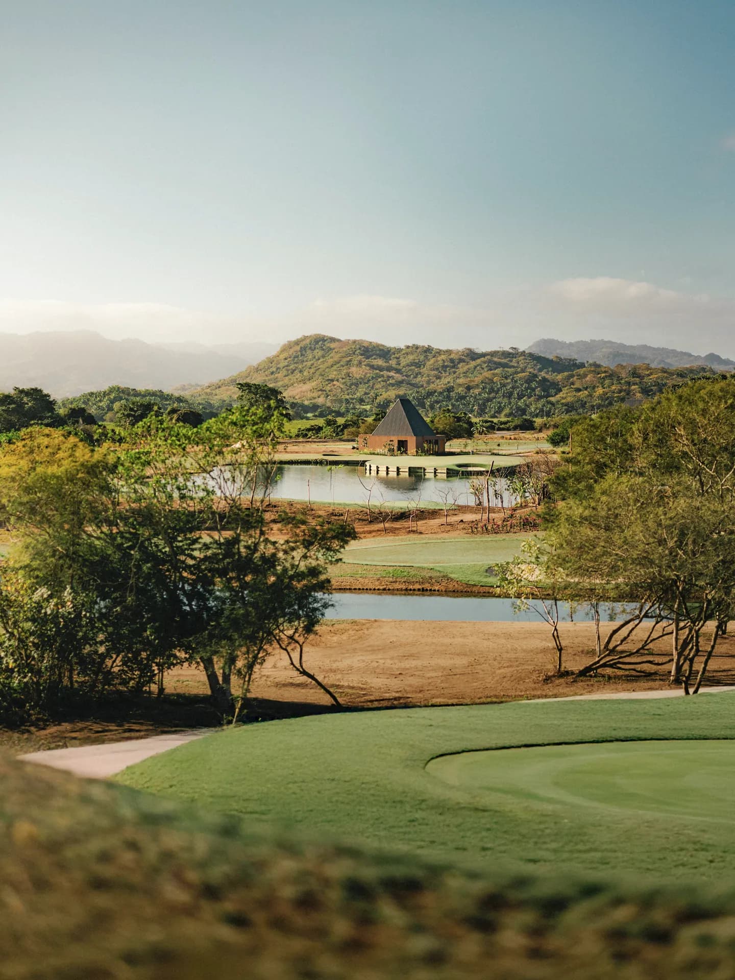 Vista del campo corto en Mandarina con greens par 3, espejos de agua y arquitectura contemporánea con las montañas de la Sierra de Vallejo al fondo.