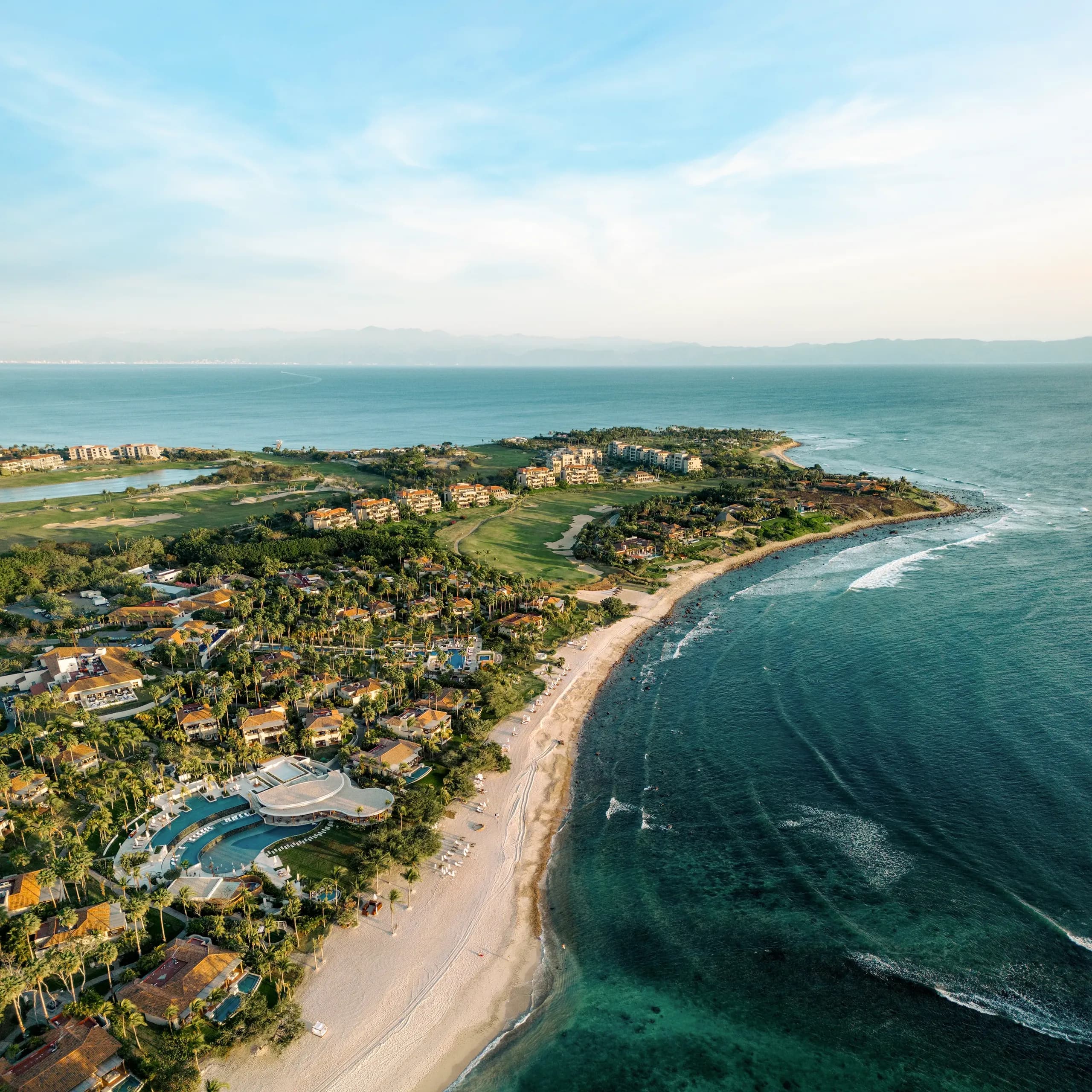 Aerial view of a luxury peninsula resort featuring beachfront villas, lush golf courses, swimming pools, and clear blue ocean waters in Punta Mita